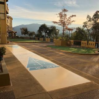A serene view of a parking area with artistic pavement design, framed by trees and mountains under a beautiful sunset.