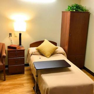 A tidy and minimalist bedroom with a single bed, lamp, chair, cabinet, and wooden flooring.