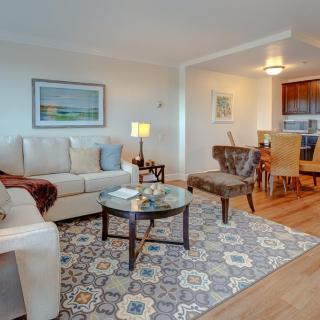 A cozy living room with a comfortable sofa, glass coffee table, and patterned rug, opening to a dining area.