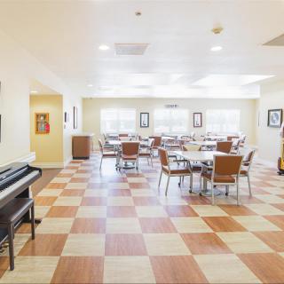 A well-lit dining area with checkered flooring, featuring multiple tables and chairs, and a piano in the corner.