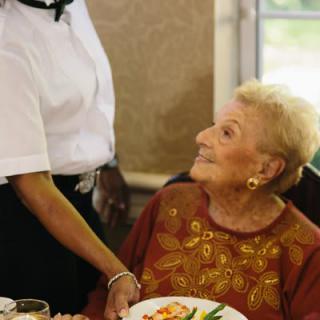 An elderly woman is being served a meal by a waitress at a restaurant.
