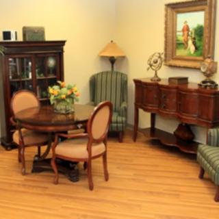 A cozy living room with classic furniture including a table, chairs, bookshelf, and a painting on the wall.