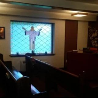 A small chapel interior featuring pews and a stained glass window depicting a religious figure.