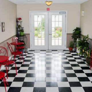 A stylish entrance area with a black and white checkerboard floor, adorned with red chairs and green plants.