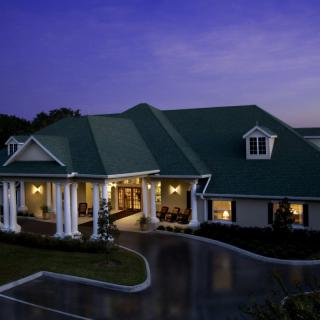 A well-lit house with a green roof and columns at dusk.