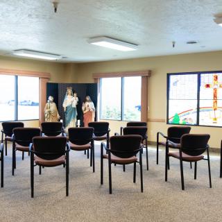 A small chapel with rows of chairs facing religious statues and windows.