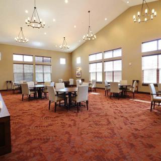 A spacious dining area with chandeliers, tables, and chairs set on a carpeted floor.