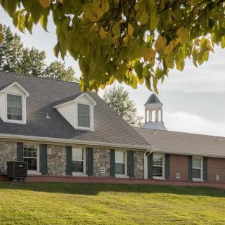 A suburban house with a well-maintained lawn and leafy trees under a clear sky.