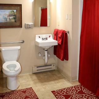 A bathroom with red accents, featuring a sink, toilet, and mirror.