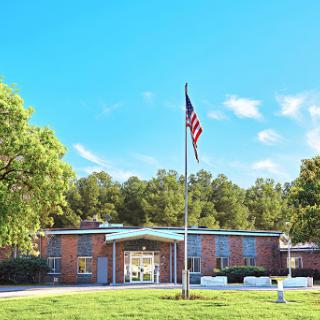 A school building with an American flag waving in front, surrounded by greenery.