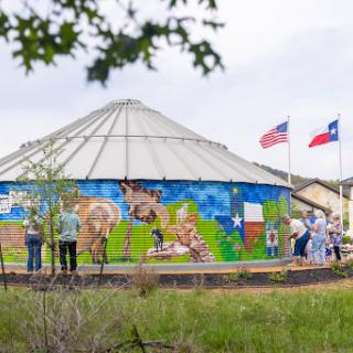 Visitors admire a vibrant mural on a round building, showcasing local culture and community spirit.