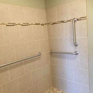 A bathroom shower with tiled walls and safety handrails.