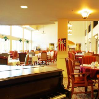 A spacious restaurant dining area with a piano and neatly arranged tables and chairs.