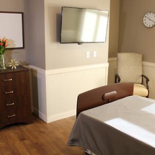 A bright and comfortable hospital room featuring a patient bed, a television for entertainment, and decorative flowers.