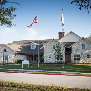 A stone building with two flags flying in front, surrounded by a well-maintained lawn.