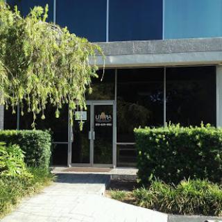 The entrance of a modern office building featuring a glass facade and well-maintained landscaping.