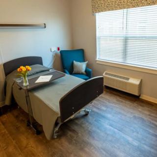 A tidy hospital room featuring a bed, a comfortable chair, and a window allowing natural light in.