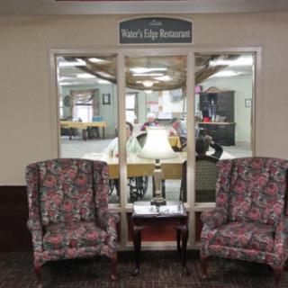 A cozy waiting area featuring two patterned armchairs and a small table, situated in front of a window leading to another room.