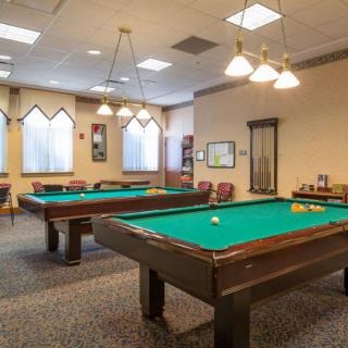 A well-lit game room featuring multiple billiards tables and comfortable seating.
