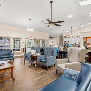 A spacious and modern living area featuring comfortable seating with blue and beige chairs, a wooden floor, and a ceiling fan for added comfort.