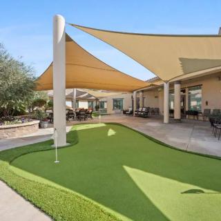 A sunny outdoor area featuring a putting green with shade sails and a patio.