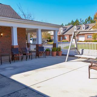 A sunny patio area with chairs and a swing, surrounded by suburban homes.