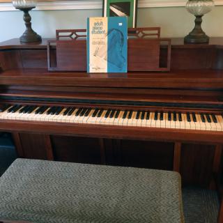 An upright piano with a music book placed on the stand, accompanied by a cushioned bench.