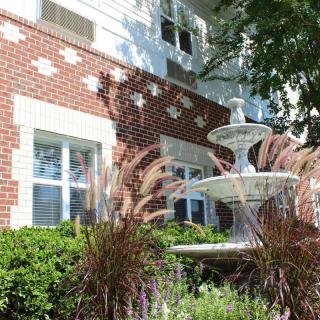 A brick building with a decorative fountain and lush greenery in the foreground.