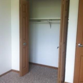 Empty closet with open wooden doors and carpeted floor.