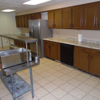A commercial kitchen with wooden cabinets, stainless steel appliances, and a tiled floor.