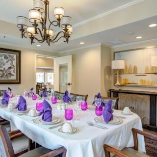 A well-decorated dining room with a table set for guests, featuring elegant purple napkins and a stylish chandelier.