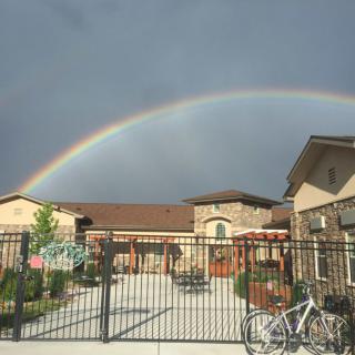 A vibrant rainbow arcs over a residential area, highlighting the contrast against the cloudy sky.