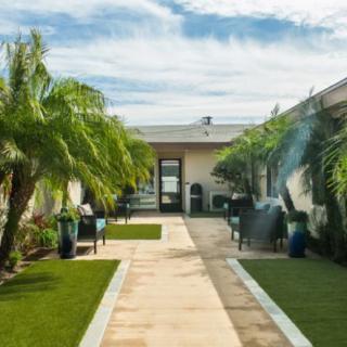 A modern courtyard featuring landscaped gardens and a central pathway lined with palm trees.