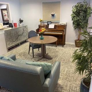 A cozy living room with a piano, round table, and comfortable seating surrounded by indoor plants.