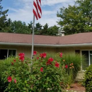 A suburban house with a well-maintained garden featuring red flowers and an American flag in front.