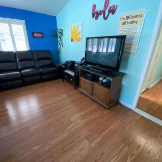 A cozy living room with a television, leather couch, and colorful wall decor.