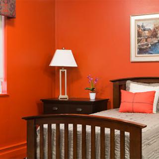 A modern bedroom featuring vibrant orange walls, a cozy bed adorned with pillows, and a stylish lamp.