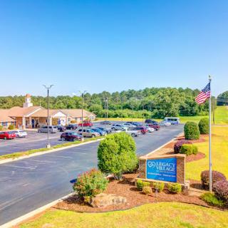 A scenic view of a building with a spacious parking lot, surrounded by greenery under a clear blue sky.