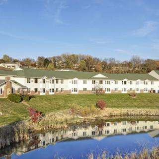 A scenic view of a building reflected in a calm pond with a blue sky backdrop.