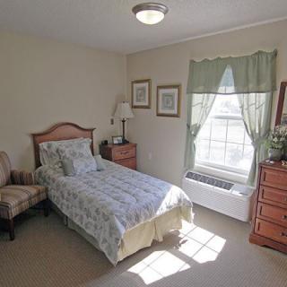 A cozy bedroom with a single bed, wooden furniture, and a window letting in natural light.