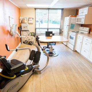 A multi-functional rehabilitation room featuring exercise equipment, a kitchenette, and a workspace.