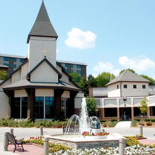 A scenic view of a building with a distinctive tower and a fountain in the foreground, set against a clear blue sky.