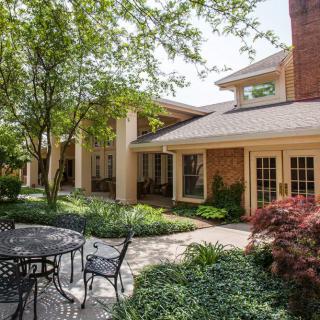 A serene garden patio area with outdoor seating surrounded by lush greenery and a charming house exterior.