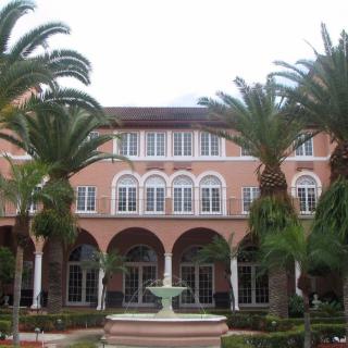 A Mediterranean-style building with palm trees and a fountain in front.