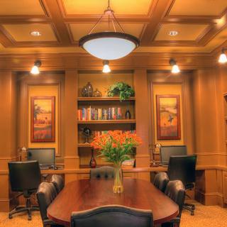 A luxurious conference room with wood paneling, a large meeting table, and comfortable chairs, adorned with artwork and a bookshelf.
