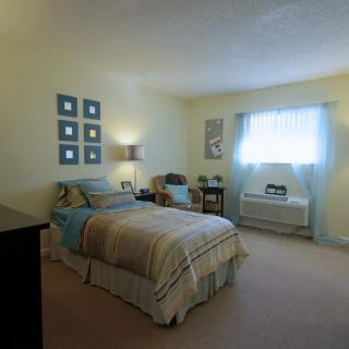 A cozy bedroom with light-colored walls and furnishings, featuring a bed, side tables, and a window.