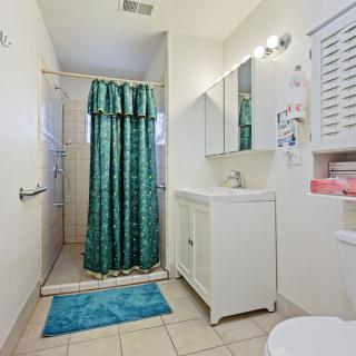 A clean bathroom with a shower, sink, and mirror, featuring teal curtains and a bath mat on the tile floor.