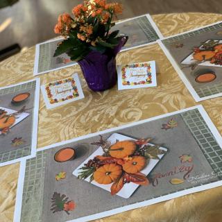 A dining table set with orange-themed placemats and a floral centerpiece in a purple pot.