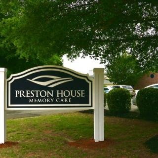 A sign for Preston House Memory Care surrounded by greenery.