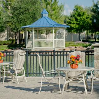 A serene outdoor setting featuring a gazebo, decorated tables with flowers, and a tranquil lake view.